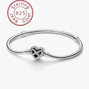 Könnte beinhalten: Ein Armband aus Sterlingsilber mit einem herzförmigen Anhänger, der ein Unendlichkeitszeichen darstellt. Der Anhänger ist mit kleinen, klaren Edelsteinen besetzt. Das Armband hat ein Schlangenketten-Design und einen Verschluss. Ein roter Kreis mit dem Text "Sterling 925 Silver".