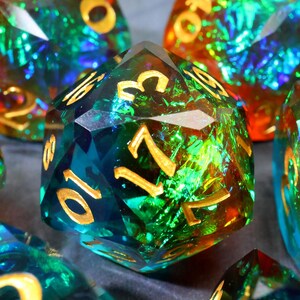 May include: Close-up of several polyhedral dice. The dice are a mix of green, blue, and orange with gold-colored numbers. The dice have a faceted, gem-like appearance, with a shimmering, iridescent quality.