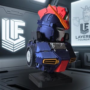 May include: A detailed model of a robot head, featuring a color scheme of navy blue, red, and white. The model has a futuristic design with visible mechanical details. The logo "LF" is displayed on the left, and the text "LAYERED - FOUNDRY" is on the right.