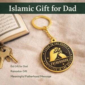 May include: Gold-colored keychain with a black and gold pendant. The pendant features the words "TOUGH IN THE DUNYA" and "FATHERHOOD PRICELESS IN THE AKHIRAH". The keychain is next to a book and keys. Text on the image reads "Islamic Gift for Dad".