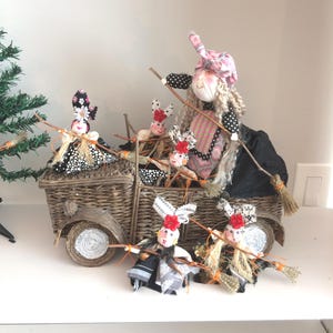 May include: A whimsical Halloween decoration featuring a woven basket designed as a vehicle, carrying several witch dolls. The dolls wear various outfits, including black and white polka dots, and hold miniature brooms. The witch dolls have red flower accents.