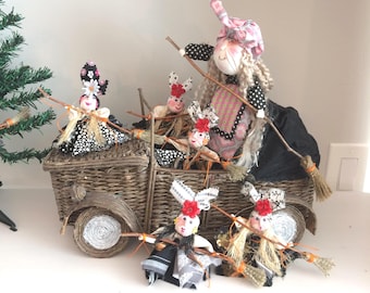 May include: A woven wicker truck figurine carrying five fabric dolls with yarn hair, each holding a small twig broom. The dolls wear patterned dresses in black, white, and pink, with floral accents. The truck features round wheels and a black fabric cover.