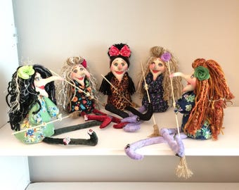 May include: Five handcrafted fabric dolls with long noses, yarn hair, and floral or patterned clothing. Each doll features a unique hair color, including black, gray, brown, and orange, and holds a thin wooden stick. They have painted faces.