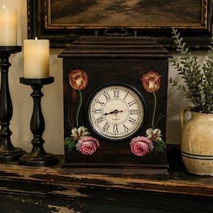 May include: A dark brown wooden mantel clock with a central circular face featuring black Roman numerals and hands. The clock case is decorated with hand-painted floral motifs including red tulips and pink roses on either side of the clock dial.