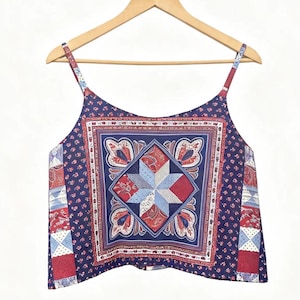 May include: A sleeveless crop top featuring a dark blue base with a central square panel displaying a light blue and red star pattern. The garment includes thin shoulder straps and side panels with a small-scale floral and geometric print.