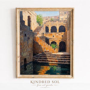 May include: A framed art print depicting an ancient stepwell with stone architecture. The artwork features a series of descending steps leading to a pool of water, with warm, earthy tones and a touch of greenery. The print is from Kindred Sol fine art prints.