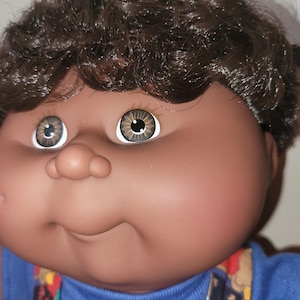 May include: A set of three ceramic mugs with a speckled, matte finish. Each mug features a different color: light blue, cream, and gray. The mugs have a simple, modern design with a rounded shape and a comfortable handle.