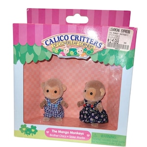 May include: Calico Critters set featuring two Mango Monkeys, Brother Chico and Sister Marita, in a decorative box. Brother Chico wears a blue and white checkered outfit, while Sister Marita is in a dark blue floral dress.