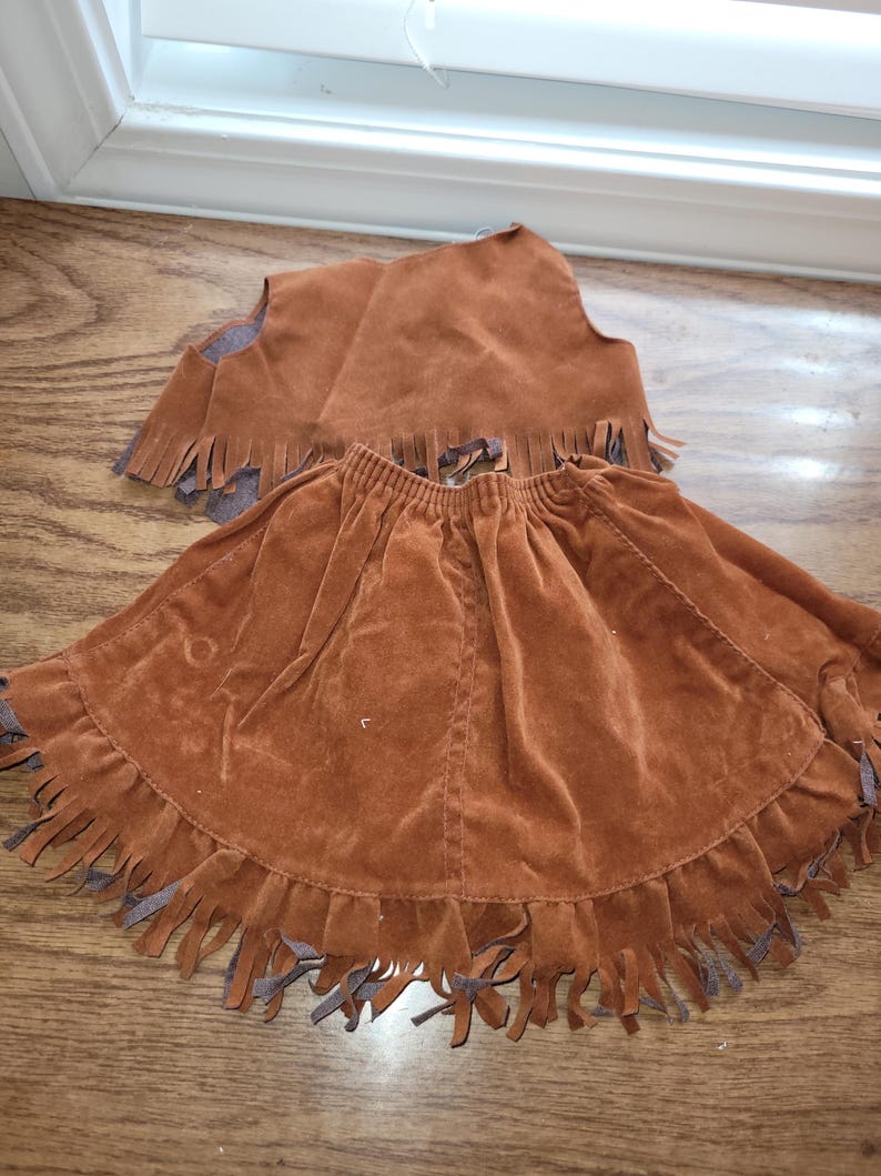 Op de afbeelding: Een bruine su&egrave;de rok en vest set. De rok heeft een gefranjerde zoom. Het vest is mouwloos met franjes langs de onderkant. De set is gemaakt van een zacht, su&egrave;de-achtig materiaal.