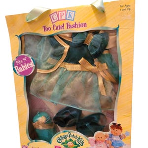 May include: A boxed Cabbage Patch Kids Babies fashion set. The set includes a teal dress, jacket, shoes, and hat with gold accents. The packaging reads "Too Cute! Fashion" and "Fits 14" Babies!"