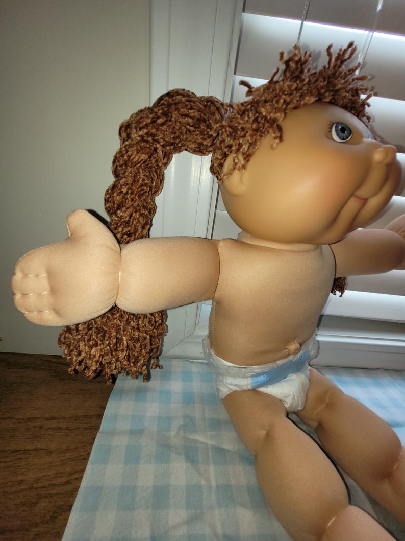 Puede incluir: Una mu&ntilde;eca vintage con tez bronceada, ojos azules y cabello casta&ntilde;o peinado en dos coletas. La mu&ntilde;eca lleva un pa&ntilde;al. Los brazos de la mu&ntilde;eca est&aacute;n extendidos.