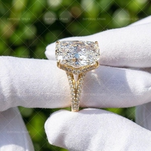 May include: A gold ring featuring a large, rectangular cushion-cut center stone with a faceted surface. The band and the setting are encrusted with small, round pavé-set stones, creating a continuous sparkling effect along the metal structure.