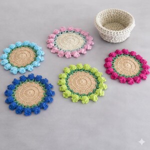 May include: A collection of handmade crochet coasters in various colors, including blue, pink, green, and blue. Each coaster features a central tan circle surrounded by a ring of colorful bobbles. A matching crochet basket is also present.