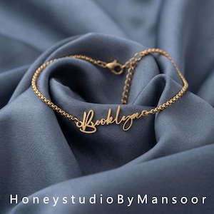 May include: A gold-toned metal chain bracelet featuring a central nameplate with the name Brooklynn written in a cursive script font. The bracelet includes a delicate box chain design and a small lobster claw clasp with an adjustable extender chain.
