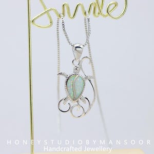May include: A silver necklace with a turtle pendant. The pendant features an oval, opalescent stone set within a detailed silver turtle design. The necklace hangs from a delicate silver chain, with the word "smile" in gold in the background.