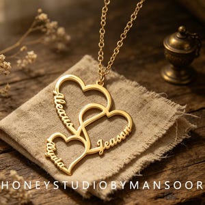 May include: A gold-toned necklace featuring a pendant composed of three interconnected heart outlines. Each heart frame is engraved with a name: Aleacus, Alyuta, and Jeason. The pendant hangs from a delicate gold-toned chain link necklace.