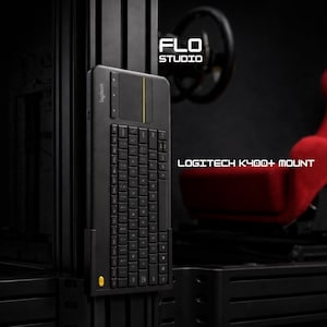Puede incluir: Soporte de teclado Logitech K400+ negro. El teclado tiene un panel táctil integrado y una raya amarilla. Los textos "FLO STUDIO" y "LOGITECH K400+ MOUNT" son visibles. El fondo incluye un asiento de carreras rojo y un marco negro.