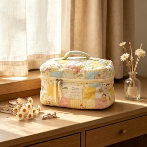 May include: A rectangular quilted cosmetic bag featuring a patchwork pattern of yellow, blue, and pink pastel squares with small floral and character illustrations. It has a top handle, a zippered closure with two fabric pulls, and a white label.