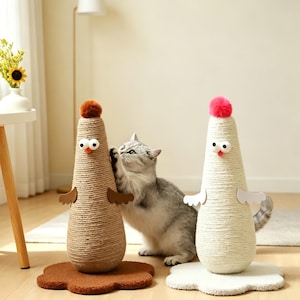 May include: Two cat scratching posts shaped like chickens. One is tan with a brown pom-pom, the other is white with a pink pom-pom. Both have googly eyes, wings, and are on a brown and white base. A gray cat is interacting with one.