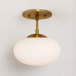 May include: A semi-flush mount ceiling light featuring a circular brass canopy and a central rod that supports a large, rounded, opaque white glass globe shade. The fixture has a metallic brass finish on the hardware and a smooth, matte white glass.