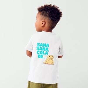 May include: White t-shirt featuring the turquoise text "SANA SANA COLA DE..." and a cartoon animal illustration. The t-shirt is worn by a child. The illustration is of a light brown animal.