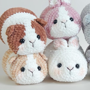 May include: A collection of four plush crochet animals made from soft, textured yarn. Two guinea pigs with brown and white patches are stacked vertically, while two round, fluffy rabbits in pink and white sit beside them, all featuring black eyes.