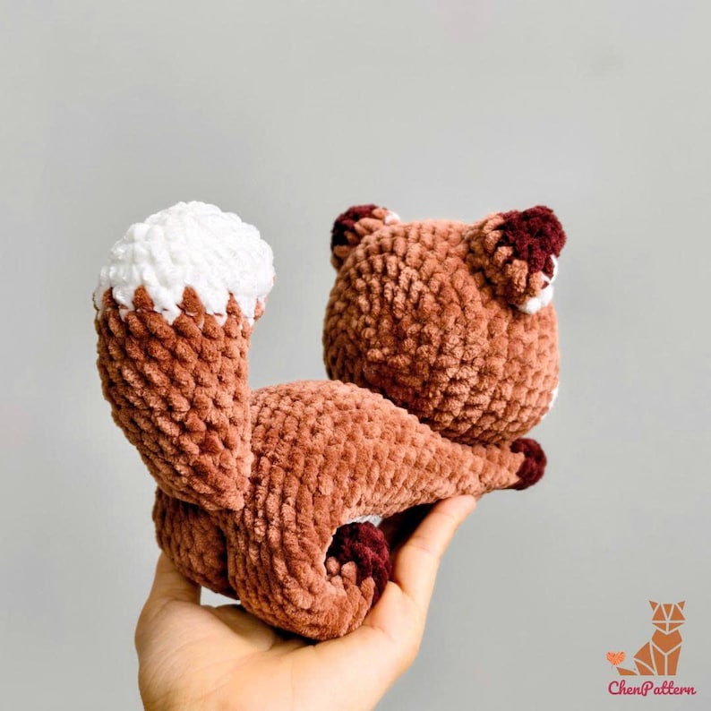 May include: A handmade crochet fox toy in shades of brown and white. The fox has a fluffy tail with a white tip and dark brown accents on the ears and paws. The toy is soft and plush, perfect for a child's room or as a decorative item.
