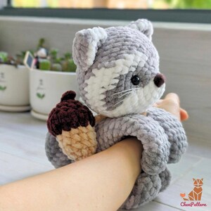 K&ouml;nnte beinhalten: Ein handgefertigtes, geh&auml;keltes Katzenspielzeug in Grau und Wei&szlig; mit einer braunen und beigen Eichel. Die Katze hat schwarze Augen und eine braune Nase. Das Spielzeug wird in der Hand einer Person gehalten.