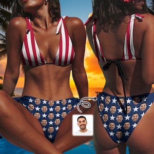 May include: A two-piece bikini set featuring a top with vertical red and white stripes and tie-shoulder straps. The bikini bottom is navy blue with a repeating pattern of white stars and a small portrait of a man's face printed on the fabric.