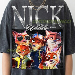 May include: Dark gray t-shirt featuring a graphic of Nick Wilde from Zootopia. The design includes the name "NICK Wilde" in silver lettering and images of Nick Wilde in various poses. The shirt has a crew neck and short sleeves.