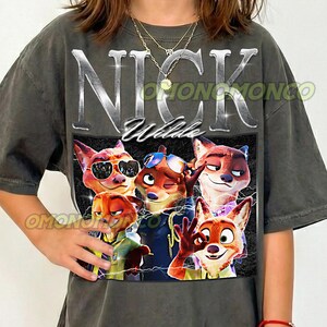 May include: Dark gray t-shirt featuring a graphic of Nick Wilde from Zootopia. The design includes the name "NICK Wilde" in silver lettering above a group of cartoon foxes. The shirt has a vintage, worn look.
