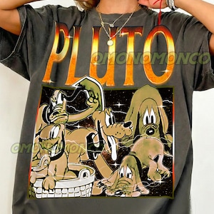 Può includere: T-shirt grigio scuro con grafica di Pluto. La parola "PLUTO" è in grandi lettere arancioni e gialle sopra un'immagine a cartoni animati di Pluto in varie pose. La maglietta ha i testi "OMONOMONCO" e "Pepper" stampati.