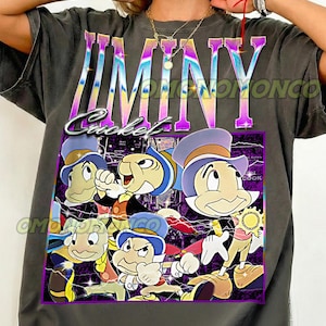 May include: Dark gray t-shirt featuring a graphic of Jiminy Cricket and other characters. The word "JIMINY" is printed across the top in a colorful, iridescent font, with "Cricket" below. The design includes the text "Original design by OMONOMONCO" and "Pepper".