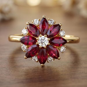 May include: A gold ring featuring a flower design. The ring's petals are made of deep red gemstones, with a central white gemstone and smaller white gemstones between the petals. The ring is set on a gold band.
