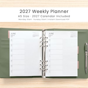 May include: An open A5 size 2027 weekly planner with a sage green cover and a silver six-ring binder mechanism. The white pages feature a grid layout for June 2027, including dates, days of the week, and a small monthly calendar. A silver pen is attached.