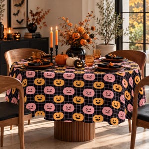 May include: A round table covered with a black and gray plaid tablecloth featuring a repeating pattern of orange and pink jack-o'-lanterns. The table is set with black plates, black napkins, and amber-colored glasses.