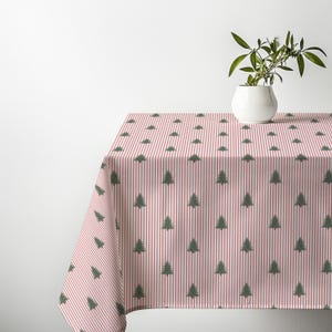 May include: A rectangular tablecloth featuring a repeating pattern of small green pine trees arranged in vertical rows against a background of thin, alternating white and red stripes. A white ceramic pot with a green plant sits on top.