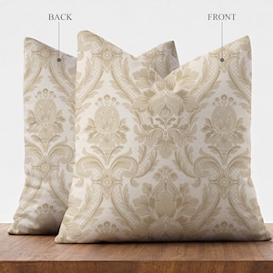 May include: Two decorative throw pillows with a beige and cream damask pattern. The pillows are square-shaped and rest on a wooden surface. The front and back of the pillows are visible, with the word "BACK" and "FRONT" labeling the sides.