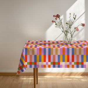 May include: A rectangular tablecloth featuring a vibrant, multi-colored grid pattern of vertical and horizontal stripes in shades of orange, purple, pink, blue, yellow, and green. Two clear glass vases containing flowers sit on the surface.