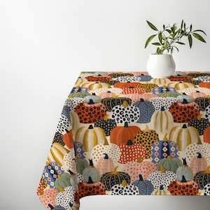 May include: A rectangular tablecloth featuring a repeating pattern of pumpkins in various colours and textures, including orange, blue, white, and yellow, with leopard print, polka dot, and geometric designs, topped with a white ceramic vase.