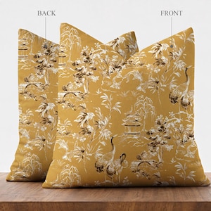 May include: Two square throw pillows in a mustard yellow fabric featuring a white and dark brown toile-style print. The pattern depicts scenes with cranes, koi fish, bamboo, trees, and pagodas. One pillow is labeled BACK and one is FRONT.