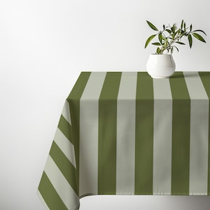 Puede incluir: Un mantel rectangular que presenta un patrón de rayas verticales repetitivas en tonos alternos de verde oliva y gris claro. La tela tiene un tejido fino y sutil visible en toda la superficie, que cae sobre el borde de una mesa.