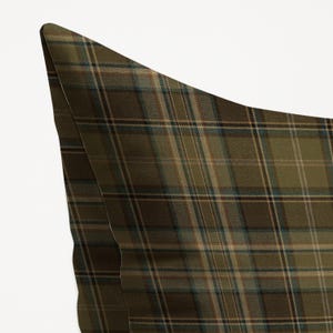 Puede incluir: Primer plano de una almohada con estampado de cuadros. La tela presenta un patr&oacute;n repetitivo de l&iacute;neas que se cruzan en tonos verde oliva, marr&oacute;n y azul. La esquina de la almohada es visible sobre un fondo blanco.