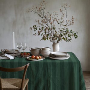 May include: A dining table set with tableware, including plates, bowls, and glasses, on a dark green striped tablecloth. A vase of flowers and a wooden chair are also present. The scene suggests a meal.