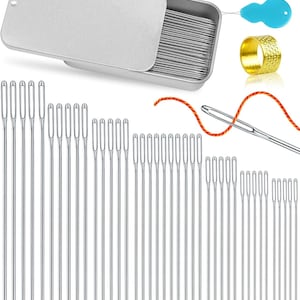 May include: A collection of sewing needles in various sizes, displayed with a metal tin, needle threaders, and a gold thimble. The needles are silver, and the threaders are red and blue. An orange thread is shown threaded through a needle.