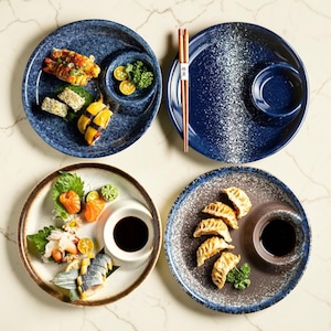 May include: Four ceramic plates with sushi and dumplings. The plates are blue, brown, and white with a speckled design. Each plate has a small, attached bowl for dipping sauce. Chopsticks are included.