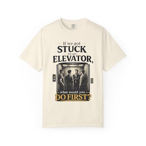 May include: Cream-coloured t-shirt with the text "If we got stuck in an elevator, what would you do first?" The graphic shows four men in an elevator. The shirt is a casual, unisex style.