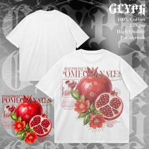Puede incluir: Una camiseta blanca de manga corta con un estampado gráfico de granadas, flores y el texto Persephone's Pomegranates. El diseño incluye una granada entera, una granada partida por la mitad y elementos botánicos. 100% algodón.