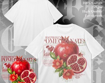 Op de afbeelding: Een wit t-shirt met korte mouwen en een grafische print van granaatappels, bloemen en de tekst Persephone's Pomegranates. Het ontwerp bevat een hele granaatappel, een gehalveerde vrucht en botanische elementen. Het shirt is 100% katoen.