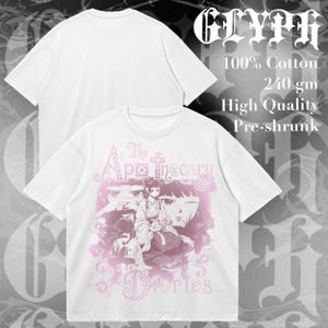 Puede incluir: Una camiseta blanca de manga corta con un estampado gráfico rosa de personajes de The Apothecary Diaries. La camiseta es de 100% algodón, 240 gm, y está preencogida. El texto GLYPH es visible en la esquina superior derecha de la imagen.